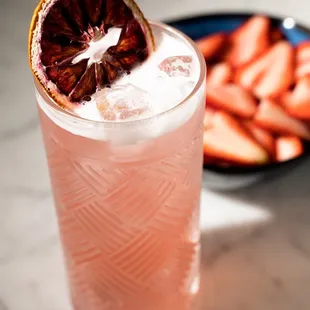 a pink drink with a slice of blood orange and strawberries