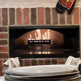 a stack of plates in front of a brick oven