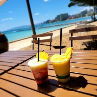 two drinks on a wooden table on the beach