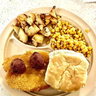 Catfish half hidden by biscuit, German fries, hush puppies and corn.