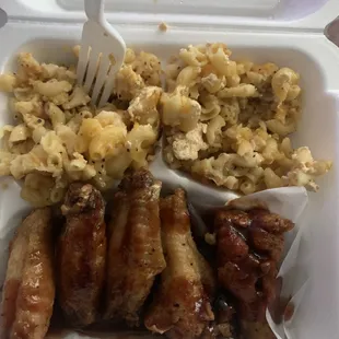 a fork in a styrofoam container filled with sausages, macaroni and cheese