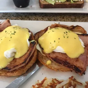 French eggs Benedict with hash browns and avocado toast with the tomatoes and onion on the side