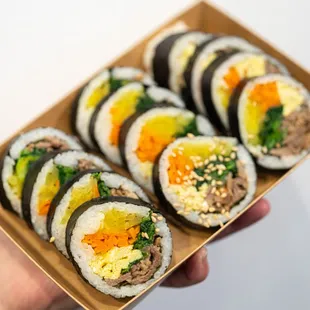 a hand holding a box of sushi rolls