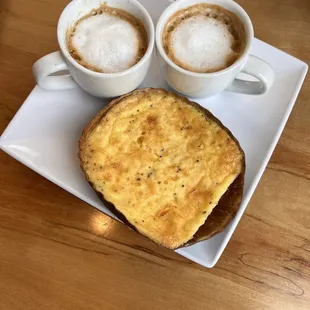 Crust free quiche and double barrel macchiatos sitting on a table next to the window on a slightly cloudy day.