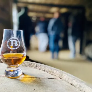 a glass of bourbon on a barrel