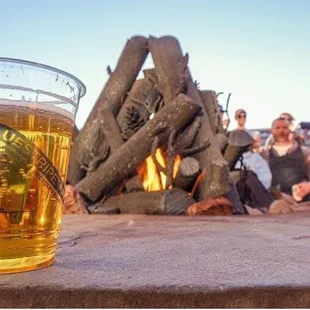 a glass of beer on a table with a fire in the background