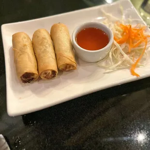 a plate of vegetable spring rolls with dipping sauce