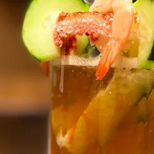 a glass of beer with shrimp, cucumber, and a slice of cucumber