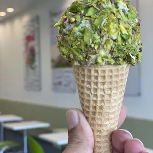 a hand holding a waffle cone with a scoop of gelato covered with