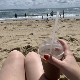a woman sitting on the beach with a drink in her hand
