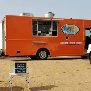 an orange food truck parked in the sand