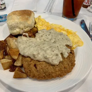 Country fried steak, eggs, home fries, and a biscuit covered in sausage gravy.
