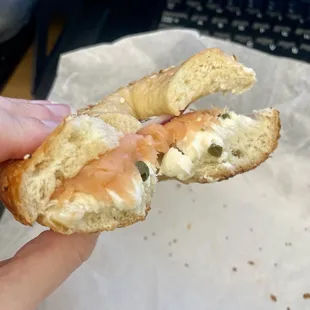 a hand holding a bagel with a bite taken out of it