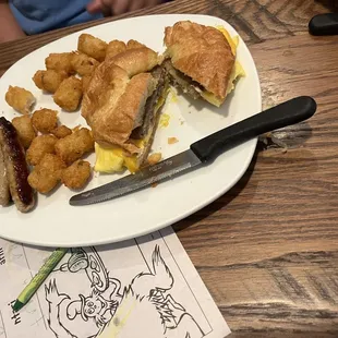 Croissant breakfast sandwich - sausage, egg, and cheese with a side of tater tots.
