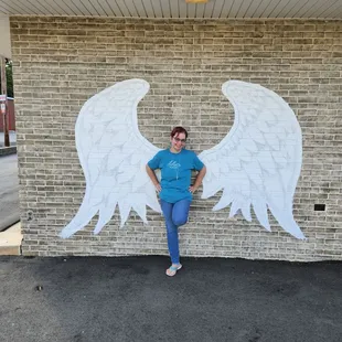 a woman leaning against a brick wall with angel wings painted on it