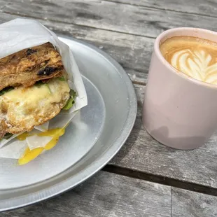 Black garlic biscuit with sausage, runny egg, microgreans, jalapeño sauce, and some other sweet sauce. Sitting next to a dirty chai!