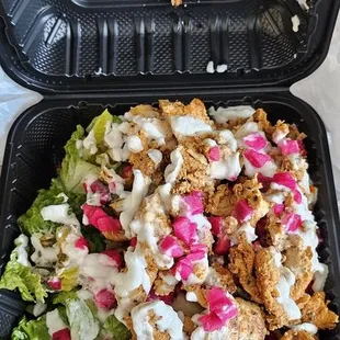 a black takeout container with a salad in it