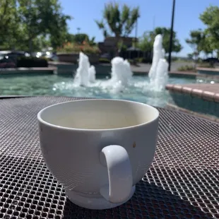 a cup of coffee on a table in front of a fountain