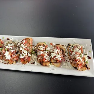 a long rectangular white plate with four pieces of bread topped with cheese and vegetables