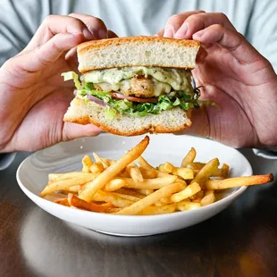 a man holding a sandwich over a bowl of fries