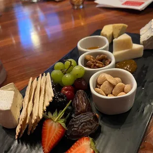 a platter of cheese, crackers, strawberries, grapes, nuts, and grapes