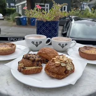 Two cups of hot chocolate, two quiche Lorraine, and three croissants on the outdoor patio at Belle Epicurean