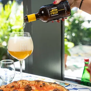 a person pouring beer into a glass over a pizza