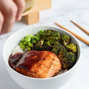 a person pouring sauce over a bowl of broccoli