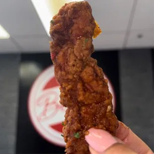 a hand holding a piece of fried chicken