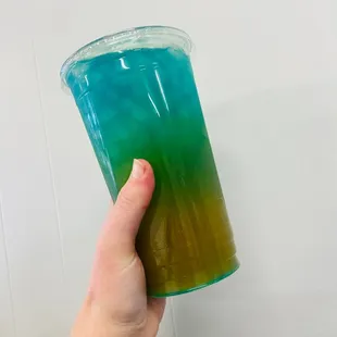 a hand holding a cup of blue and green liquid