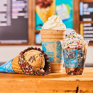 Waffle cone, shake and sundae in front of Ben &amp; Jerry&apos;s ice cream shop menu board.