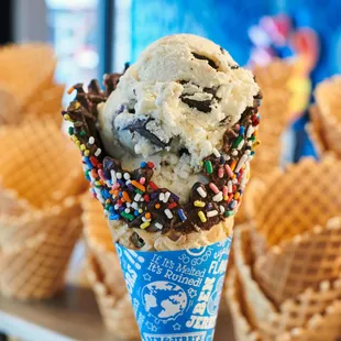 A Ben &amp; Jerry's freshly baked dipped waffle cone with sprinkles in front of waffle cone display.