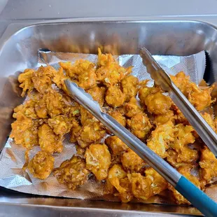 a tray of fried food with tongs