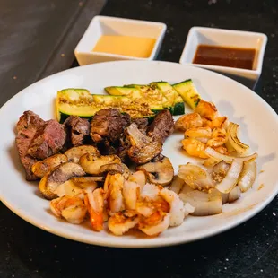 a plate of meat, vegetables, and sauces