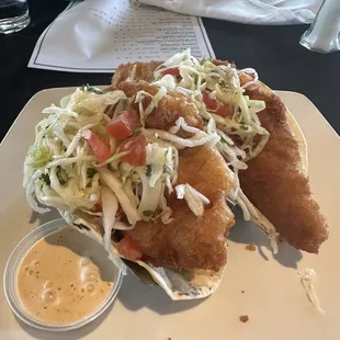a plate of fish tacos with coleslaw and sauce