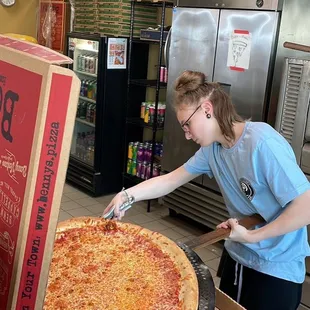 a woman cutting a large pizza