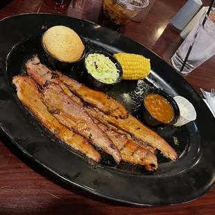 a black plate with ribs, corn, and coleslaw