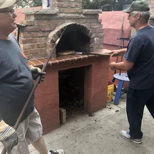 two men standing in front of a brick oven