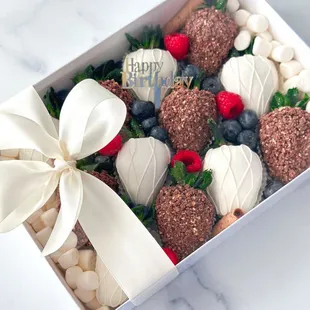 White and milk chocolate covered strawberries adorned with fresh berries and Ferrero Rocher crumbs.