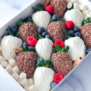 White and milk chocolate covered strawberries adorned with fresh berries and Ferrero Rocher crumbs.