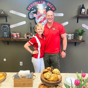 a man and a woman standing in front of a counter with pastries