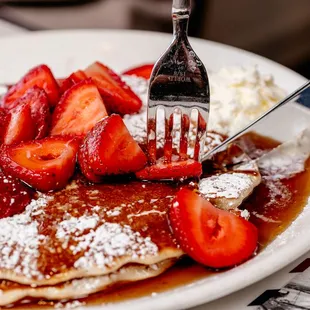 a plate of pancakes with strawberries and powdered sugar