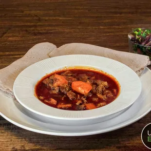 a bowl of beef stew with a side salad