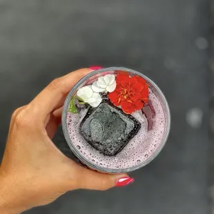 a hand holding a glass of ice cream with a flower on top