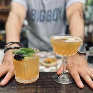 a man sitting at a bar with two cocktails