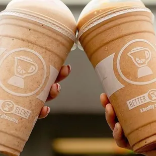 two hands holding two cups of coffee