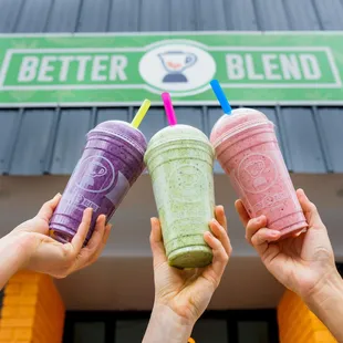 three people holding up two smoothie cups
