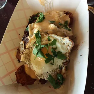 Poutine with egg, homemade tots, brisket, cheese curds blanketed with bechamel sauce; awesomeness in a paper food boat!