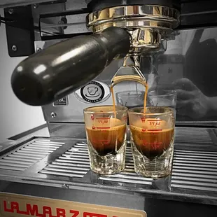 two shot glasses of coffee being poured into a coffee machine
