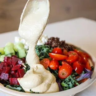 a bowl of salad with dressing being drizzled over it